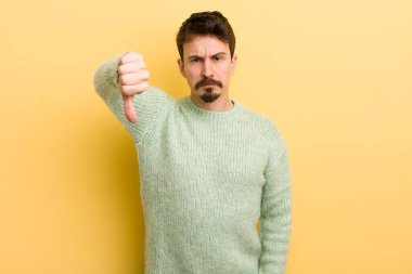 Genç İspanyol bir adam kızgın, sinirli, hayal kırıklığına uğramış ya da canı sıkkın, ciddi bir bakışla başparmağını kaldırıyor.