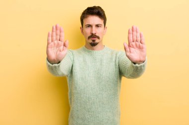 Genç İspanyol adam ciddi, mutsuz, kızgın ve hoşnutsuz görünüyor. Girmeyi yasaklıyor ya da her iki avuçta da dur diyor.