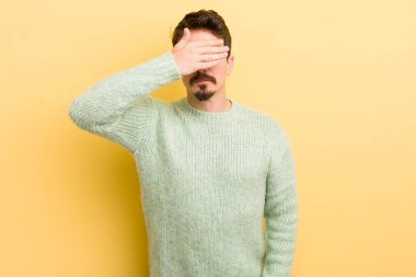 Genç İspanyol bir adam tek eliyle gözlerini kapatıyor korkmuş ya da endişeli hissediyor, merak ediyor ya da körü körüne bir sürpriz bekliyor.