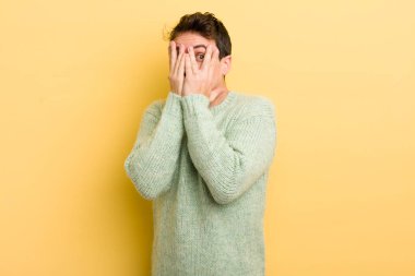 Genç İspanyol adam elleriyle yüzünü kapatıyor, parmaklarının arasından şaşkın bir ifadeyle yan tarafa bakıyor.