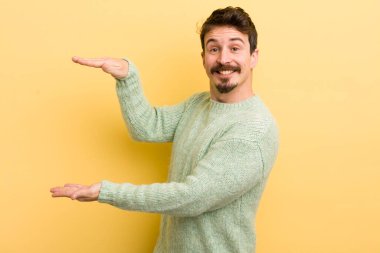 Genç İspanyol adam gülümsüyor, mutlu, pozitif ve memnun, fotokopi alanında nesne ya da konsept tutuyor ya da gösteriyor