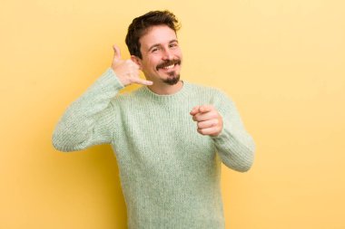 Genç İspanyol adam neşeyle gülümsüyor ve kamerayı işaret ederek seni daha sonra arıyor, telefonla konuşuyor.