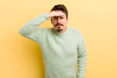 Genç İspanyol adam şaşkın ve şaşkın bakıyor, el üstünde uzak bakıyor, izliyor ya da arıyor