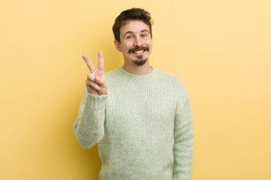 Genç İspanyol adam gülümsüyor ve arkadaş canlısı görünüyor. İki ya da iki numarayı gösteriyor. Elleri önde, geri sayıyor.