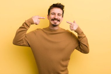 Genç İspanyol adam kendine güvenerek gülümsüyor. Geniş gülümseme, pozitif, rahat, tatmin olmuş tavır.