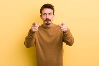 Genç Latin asıllı bir adam kamerayı iki parmağıyla ve kızgın bir ifadeyle sana görevini yapmanı söylüyor.