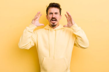 young hispanic man screaming with hands up in the air, feeling furious, frustrated, stressed and upset