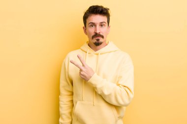 Genç İspanyol adam mutlu, pozitif ve başarılı hissediyor, göğsünün üzerinde el yapımı V ile zafer ya da barış gösteriyor.