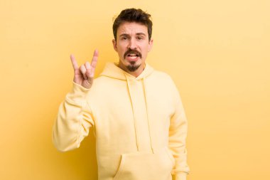 Genç İspanyol adam kendini mutlu, eğlenceli, kendinden emin, pozitif ve asi hissediyor, elle rock ya da heavy metal işareti yapıyor.