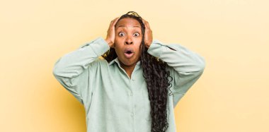 Siyahi güzel bir kadın hoş olmayan bir şekilde şok olmuş, korkmuş ya da endişeli görünüyor, ağzı sonuna kadar açık ve iki kulağını da elleriyle kapatıyor.