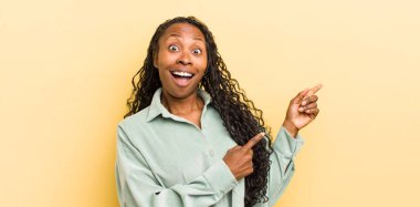 Siyah, güzel bir kadın kendini neşeli ve şaşırmış hissediyor. Şok olmuş bir ifadeyle gülümsüyor ve bir tarafı işaret ediyor.