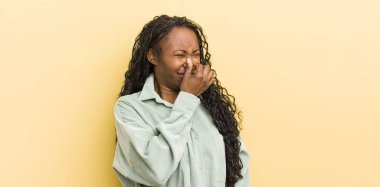 Siyahi güzel kadın iğreniyor, kötü ve nahoş bir koku duymamak için burnunu tutuyor.