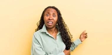 Siyah, güzel bir kadın şok olmuş ve şaşırmış hissediyor. Kenardaki fotokopi alanını işaret ediyor. Şaşırmış, ağzı açık bir bakışla.