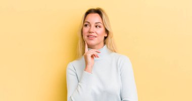 Sarışın, beyaz kadın mutlu bir şekilde gülümsüyor ve hayal kuruyor ya da şüphe ediyor.