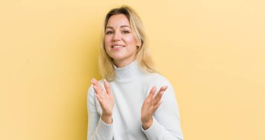 Sarışın beyaz kadın mutlu ve başarılı hissediyor, gülümsüyor ve alkışlıyor, alkışlarla tebrik ediyor.