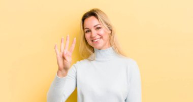 Sarışın, beyaz bir kadın gülümsüyor ve arkadaş canlısı görünüyor. Elleri önde, geriye doğru sayıyor.