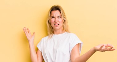 blonde caucasian woman shrugging with a dumb, crazy, confused, puzzled expression, feeling annoyed and clueless