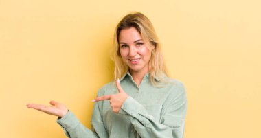 Sarışın, beyaz kadın gülümsüyor, mutlu, kaygısız ve tatmin olmuş hissediyor, fotokopi alanındaki konsept ya da fikre işaret ediyor.