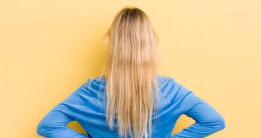 Sarışın, beyaz bir kadın kafası karışık ya da dolgun ya da şüphe ve soru dolu, merak ediyor, elleri kalçasında, dikiz aynasından