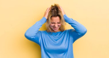 Sarışın, beyaz bir kadın stresli ve hayal kırıklığına uğramış hissediyor. El ele tutuşuyor. Yorgun, mutsuz ve migren ağrısı çekiyor.