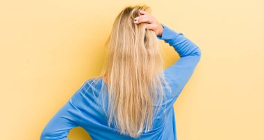 Kafası karışık ve kafası karışık sarışın bir kadın, bir çözüm düşünüyor, eli kalçasında, diğeri kafasında, dikiz aynasından.