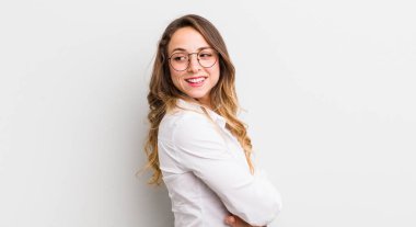 Güzel bir kadın neşeyle gülümsüyor, mutlu, tatmin olmuş ve rahatlamış hissediyor, kollarını kavuşturup yan tarafa bakıyor.