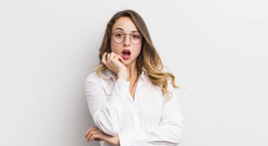 Güzel bir kadın şok ve inançsızlık içinde, elleri yanağında ve kolları çaprazlanmış, sersemlemiş ve şaşırmış hissediyor.