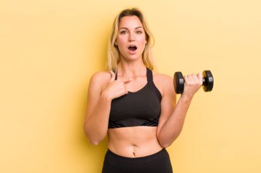 Şok olmuş ve ağzı açık, kendini işaret eden sarışın güzel bir kadın.