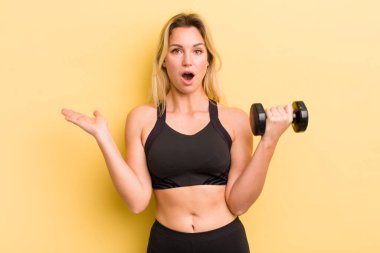 Güzel sarışın kadın şaşırmış ve şok olmuş görünüyor, çenesi düşmüş, elinde bir nesne tutuyor.