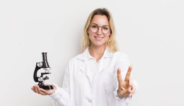 Güzel sarışın kadın gülümsüyor ve mutlu görünüyor. Zafer ya da huzur işareti yapıyor.