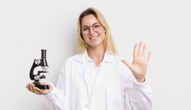 Sarışın, güzel bir kadın gülümsüyor ve arkadaş canlısı görünüyor, beş numarayı gösteriyor.