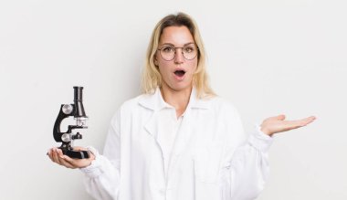 Güzel sarışın kadın şaşırmış ve şok olmuş görünüyor, çenesi düşmüş, elinde bir nesne tutuyor.