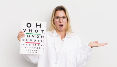 Güzel sarışın kadın şaşırmış ve şok olmuş görünüyor, çenesi düşmüş, elinde bir nesne tutuyor.