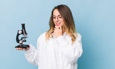 Güzel bir kadın mutlu, kendinden emin bir ifadeyle gülümsüyor, elleri çenesinde.