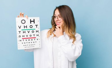 Güzel bir kadın mutlu, kendinden emin bir ifadeyle gülümsüyor, elleri çenesinde.