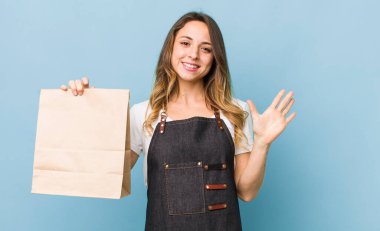 Güzel bir kadın mutlu bir şekilde gülümser, el sallar, hoş karşılar ve seni selamlar.