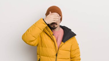 Beyaz duvarda paltosu olan genç yakışıklı bir adam.