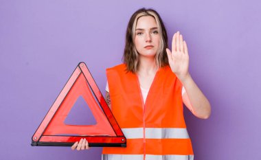 Beyaz kadın ciddi görünüyor. Avuç içinin açık olduğunu gösteriyor. Durdurma hareketi yapıyor. araba üçgeni kavramı