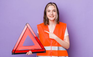 Güzel, beyaz bir kadın, neşeli bir şekilde gülümsüyor, mutlu hissediyor ve bir tarafı işaret ediyor. araba üçgeni kavramı