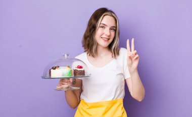 Güzel, beyaz bir kadın gülümsüyor ve arkadaş canlısı görünüyor. İki numarayı gösteriyor. Ev yapımı kek konsepti