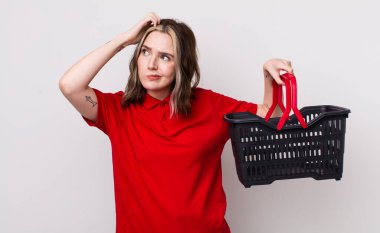 Kafası karışmış, kafası karışmış, kaşınan beyaz bir kadın. boş alışveriş sepeti kavramı