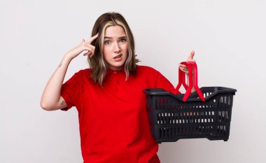 Kafası karışmış ve kafası karışmış beyaz bir kadın. Deli olduğunu gösteriyor. boş alışveriş sepeti kavramı