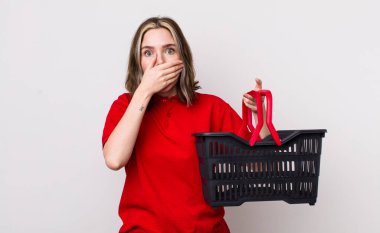 Güzel, beyaz bir kadın elleri ile ağzını kapatıyor. boş alışveriş sepeti kavramı