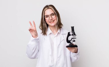 Güzel beyaz kadın gülümseyen ve mutlu görünen, zafer ya da barış işareti yapan. Mikroskop konseptine sahip bilim adamı