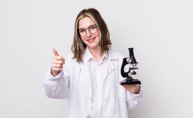 Güzel, beyaz bir kadın gururlu, olumlu gülümsüyor. Mikroskop konseptine sahip bilim adamı