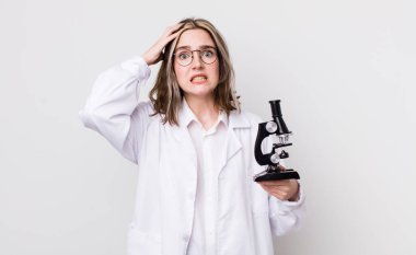 Kafkasyalı bir kadın stresli, endişeli ya da korkmuş, elleri başının üstünde. Mikroskop konseptine sahip bilim adamı