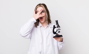 Güzel, beyaz bir kadın şok olmuş, korkmuş ya da korkmuş görünüyor. Yüzü elle kapatılmış. Mikroskop konseptine sahip bilim adamı