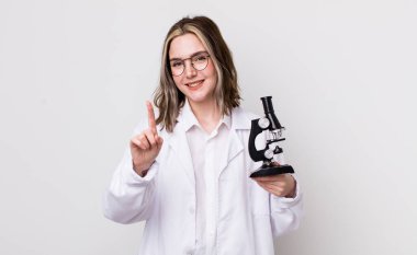 Güzel, beyaz bir kadın gururla gülümsüyor ve kendine güvenerek bir numara oluyor. Mikroskop konseptine sahip bilim adamı