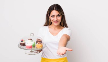 Şirin İspanyol bir kadın arkadaşça gülümsüyor ve bir konsept sunuyor. Ev yapımı kek konsepti