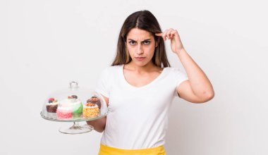 Kafası karışmış, kafası karışmış, deli olduğunu gösteren güzel İspanyol bir kadın. Ev yapımı kek konsepti